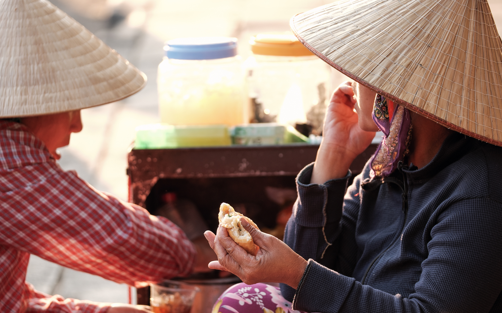 Local Vietnamese women eating baguette bread with vegetable and meat filling (called Banh My or Banh Mi in Vietnamese) - popular street food in Vietnam