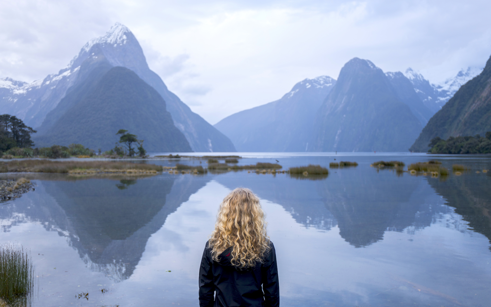 Young woman looks over the water at Milford Sound, New Zealand.