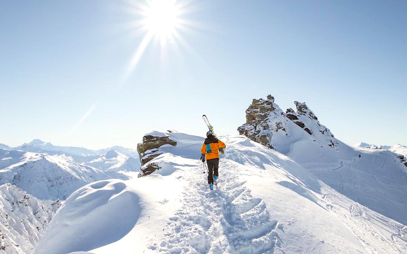 A skier walking up a snowy mountain carrying skies