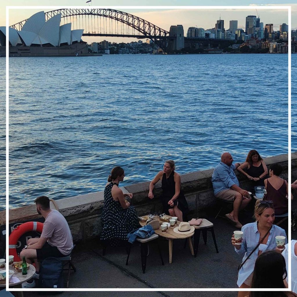 People sitting by the water overlooking the Sydney Harbour Bridge
