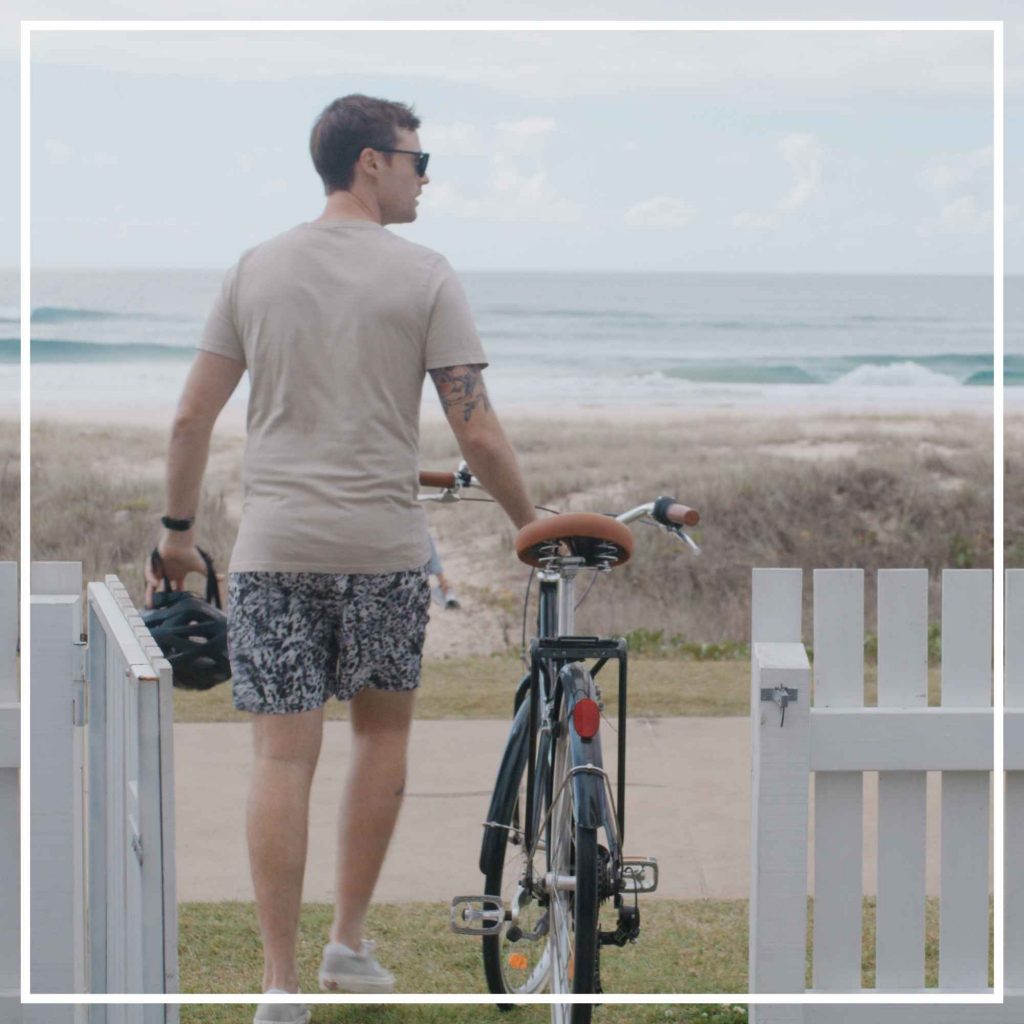 Man leading bike onto path by the beach at the Gold Coast